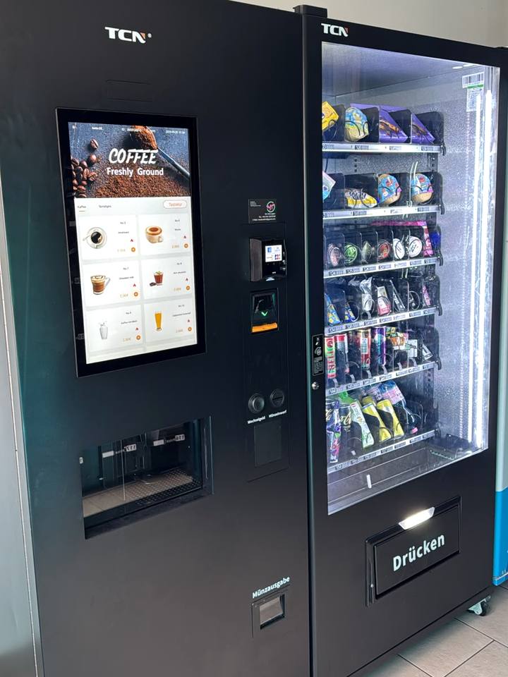 Schwarzer Kaffeeautomat mit Touchscreen neben einem Kühlautomaten